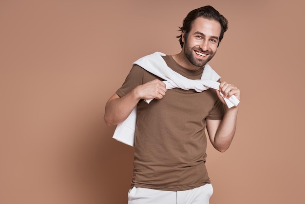 Giovane alla moda che guarda la telecamera e sorride sullo sfondo marrone