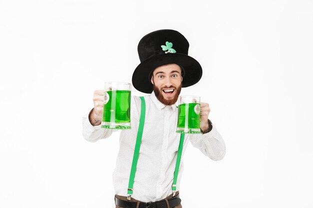 Giovane allegro che celebra il giorno di StPatrick isolato sopra il muro bianco, bevendo birra