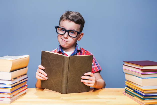 Giovane allievo in vetri che legge un libro nella biblioteca della scuola. Concetto di educazione