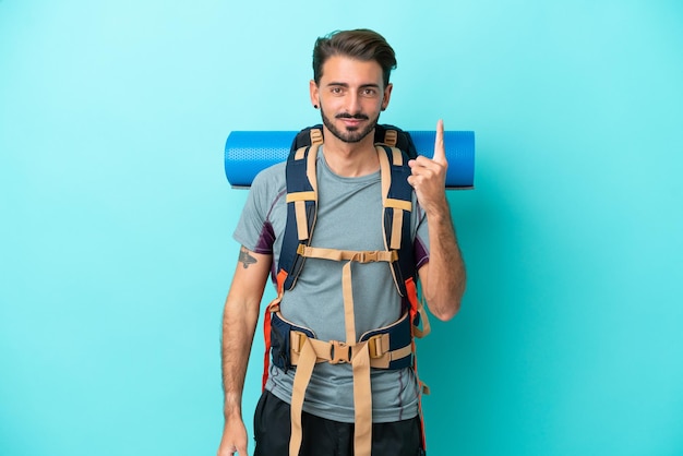 Giovane alpinista con un grande zaino isolato su sfondo blu che punta con il dito indice una grande idea