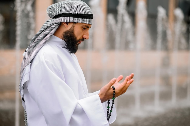 Giovane arabo barbuto in abiti tradizionali che prega