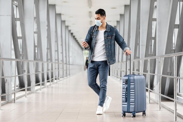 Giovane arabo che indossa una maschera medica utilizzando lo smartphone in aeroporto