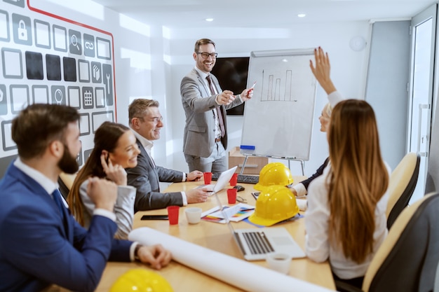 Giovane architetto caucasico di successo che parla del nuovo progetto e che risponde alle domande. Alla scrivania i suoi colleghi seduti e chiedendo di più sul progetto.