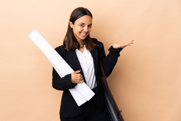 Giovane architetto donna in possesso di schemi sopra il muro che si estende le mani al lato per invitare a venire