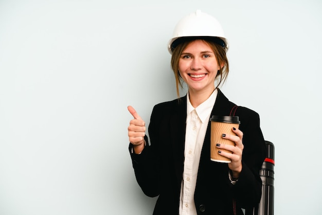 Giovane architetto donna inglese con casco e azienda progetti isolati su sfondo blu sorridente e alzando il pollice