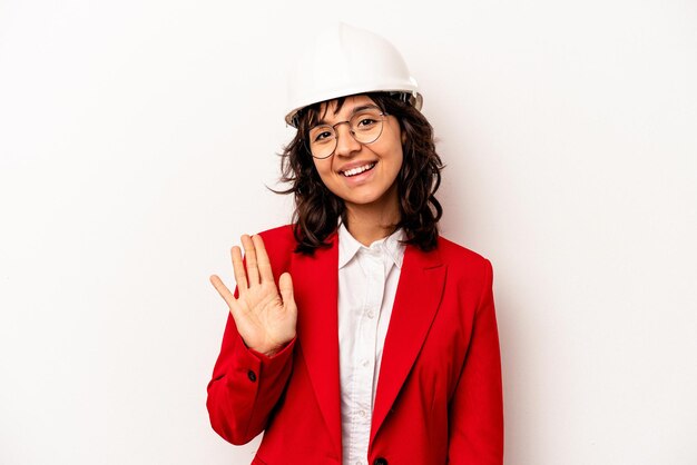 Giovane architetto donna ispanica con casco isolato su sfondo bianco sorridente allegro che mostra il numero cinque con le dita