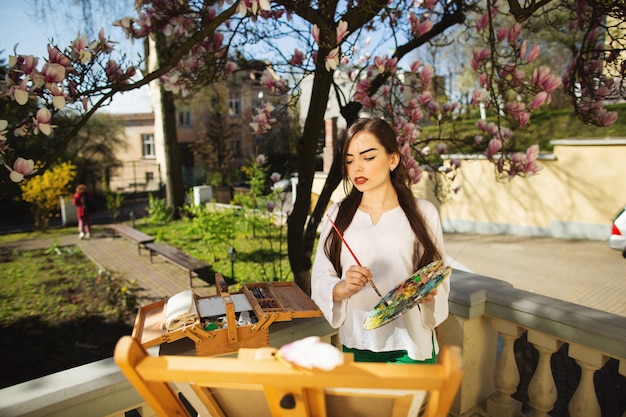 Giovane artista della donna del brunette che tiene in mani una spazzola e una gamma di colori.