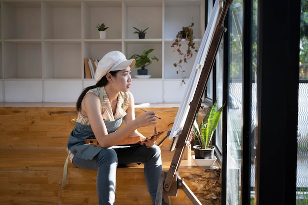 Giovane artista donna asiatica seduta davanti al cavalletto da disegno e allo studio paintingxAin