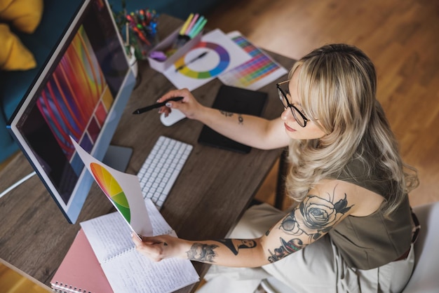 Giovane artista freelance femminile sicura che sembra premurosa mentre lavora al computer dal suo ufficio a casa.