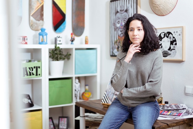 Giovane artista ragazza nel suo studio d'arte contemplando pensieroso una delle sue opere.