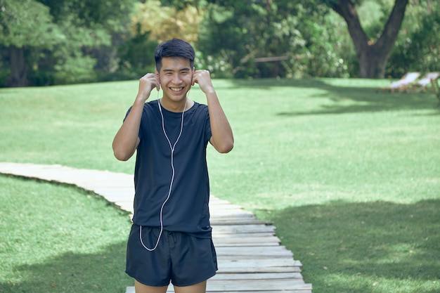 Giovane asiatico bello che si esercita nel parco che indossa un tracker di fitness