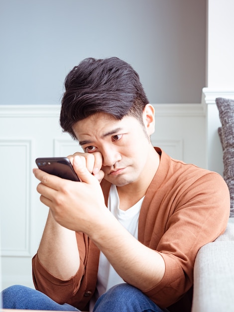 Giovane asiatico che si sfrega gli occhi stanchi il suo smartphone.