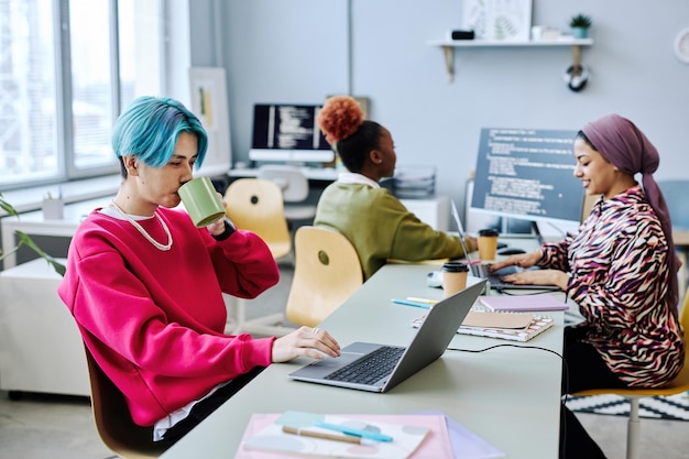 Giovane asiatico che usa il computer portatile in ufficio e beve caffè con accento magenta