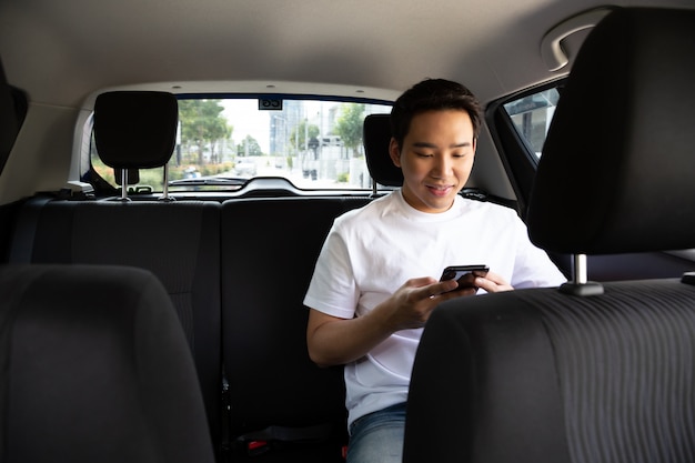 Giovane asiatico che utilizza uno smartphone nel sedile posteriore dell'automobile