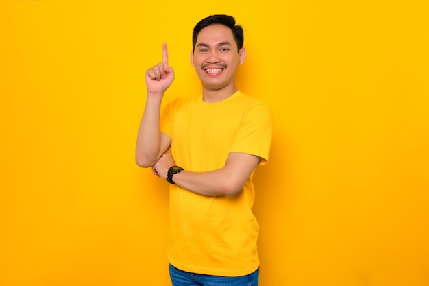 Giovane asiatico eccitato in maglietta casual che punta il dito verso l'alto avendo un'idea o una soluzione trovata isolata su sfondo giallo Concetto di stile di vita delle persone