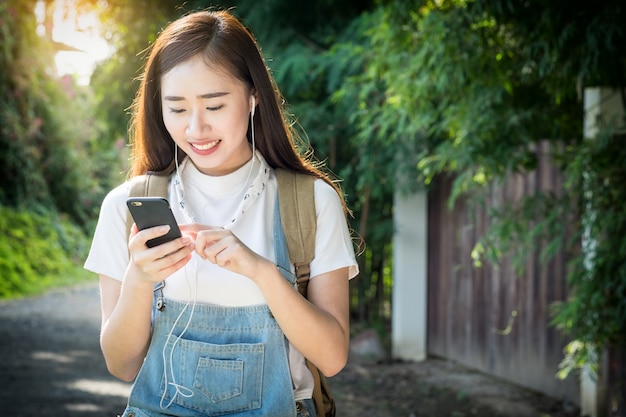 Giovane asiatico hipster indossa la cuffia che ascolta la musica attraverso smartphone in piedi all&#39;aperto sullo sfondo della natura