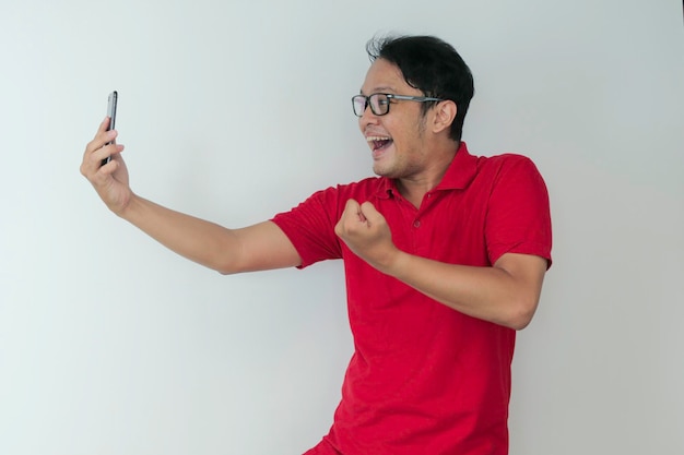 Giovane asiatico scioccato e felice di ciò che vede nello smartphone su sfondo grigio isolato
