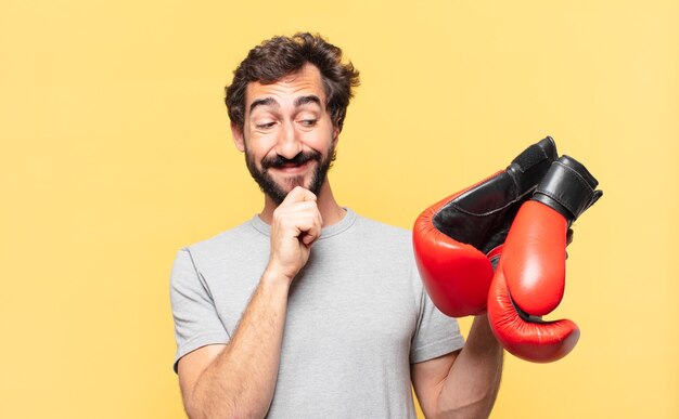 Giovane atleta barbuto pazzo che pensa espressione e tiene in mano un guantone da boxe