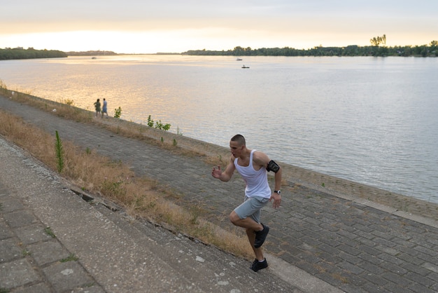 Giovane atleta bello che corre di sopra dalla sponda del fiume