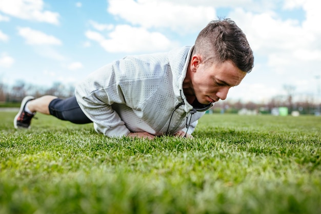 Giovane atleta che fa flessioni e fa esercizi sull'erba verde, durante l'allenamento primaverile all'esterno.