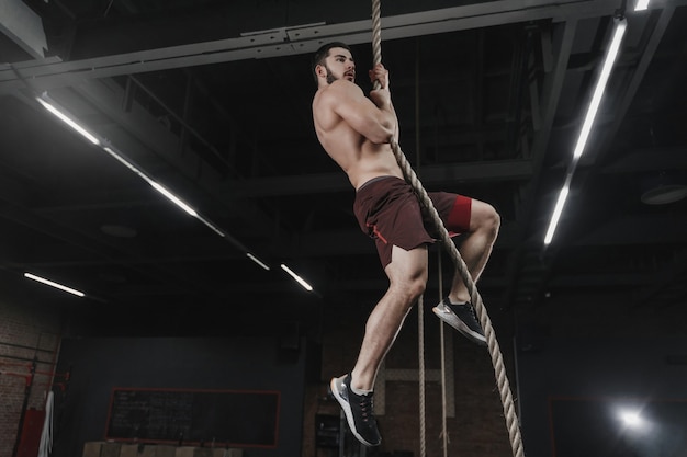 Giovane atleta crossfit arrampicata su una corda in palestra