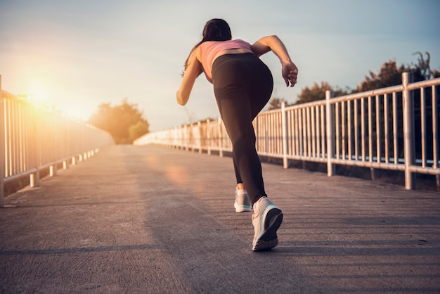 Giovane atleta del corridore della donna di forma fisica che corre sulla strada al tramonto