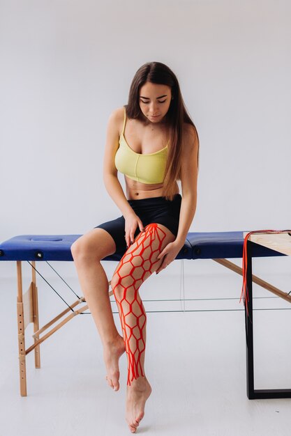 Giovane atleta femminile allegra che tiene la gamba ferita dopo il trattamento con nastro kinesio.