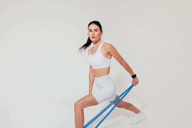 Giovane atleta femminile in abiti sportivi bianchi che utilizza una fascia di resistenza per allenare il braccio