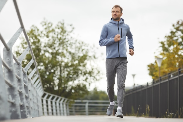 Giovane atleta in abbigliamento sportivo fare jogging da solo lungo la strada della città all'aperto