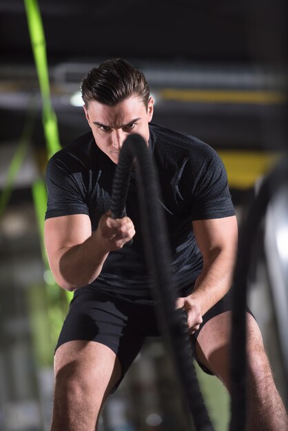 giovane atleta in forma che si allena nella palestra di allenamento funzionale facendo esercizi di corde da battaglia come parte dell'allenamento di fitness incrociato