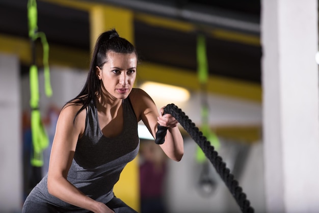 giovane atleta in forma donna che lavora in palestra di allenamento funzionale facendo esercizi di corde da battaglia come parte dell'allenamento di fitness incrociato