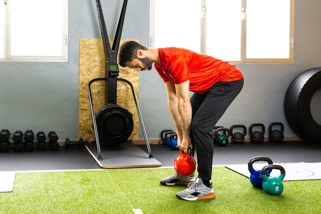 Giovane atleta maschio che afferra un kettlebell pesante sul pavimento di cemento durante l'allenamento di sollevamento pesi in palestra