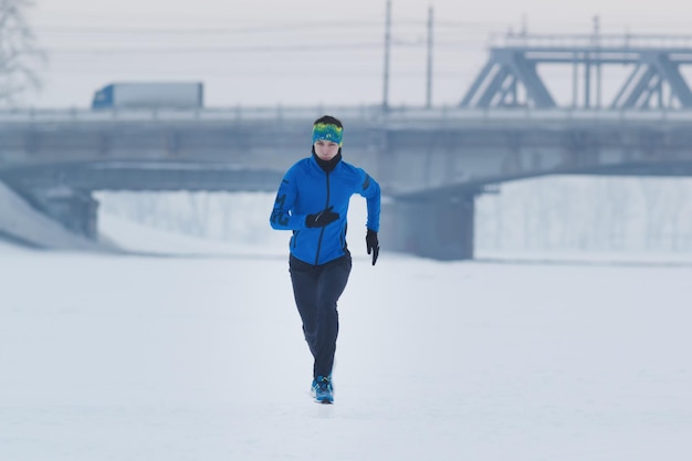 Giovane atleta maschio che corre in inverno attraverso il concetto di neve, sport e tempo libero