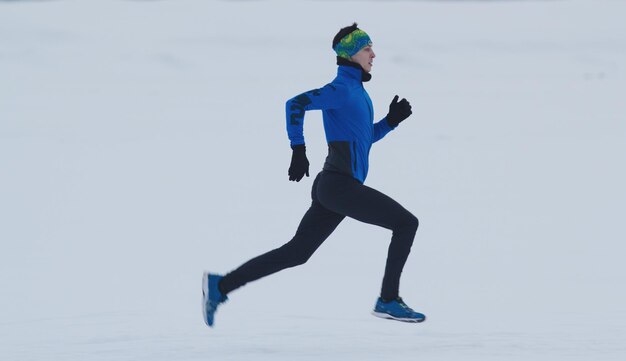 Giovane atleta maschio che corre veloce in inverno attraverso il campo di ghiaccio innevato, concetto di sport e tempo libero