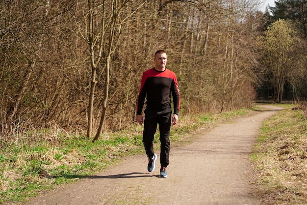 Giovane atleta maschio in abiti sportivi su un sentiero nel bosco. Un uomo dopo una corsa mattutina cammina nel bosco