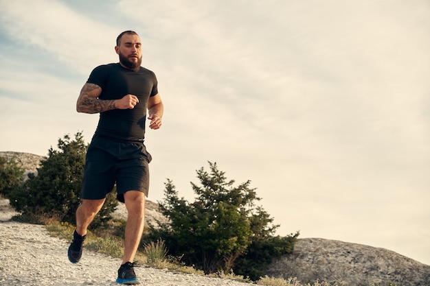 Giovane atleta maschio muscoloso che corre su per la collina