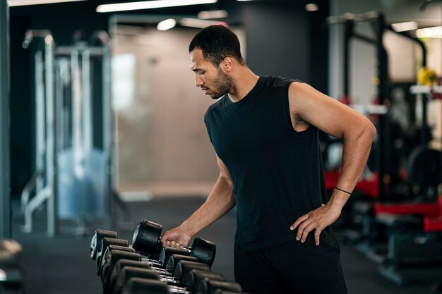 Giovane atleta maschio nero prendendo manubri in palestra scegliendo attrezzature per l'allenamento