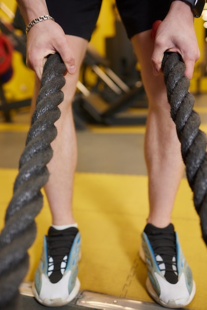 Giovane atletico con la corda di battaglia che fa esercizio nella palestra di forma fisica di addestramento funzionale
