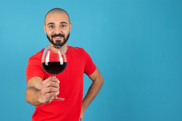 Giovane attraente che mostra un bicchiere di vino rosso.