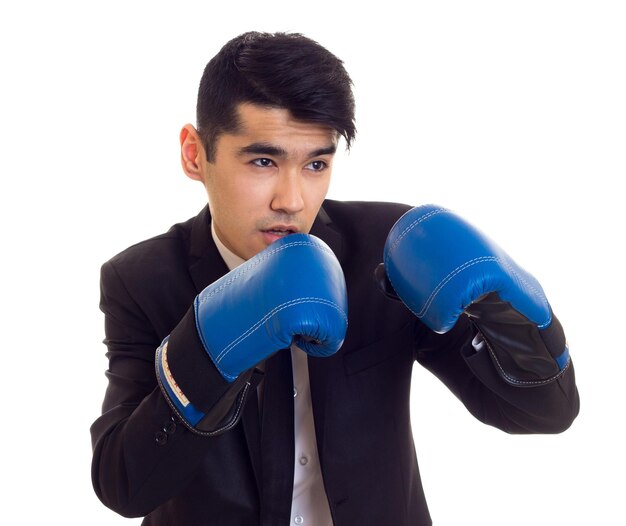 Giovane attraente con capelli neri in camicia bianca e smoking nero con cravatta e guantoni da boxe blu