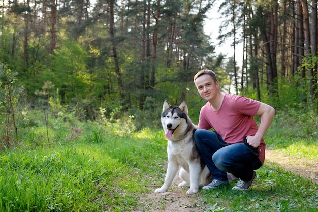 Giovane attraente con il suo malamute del cane su una passeggiata nella foresta