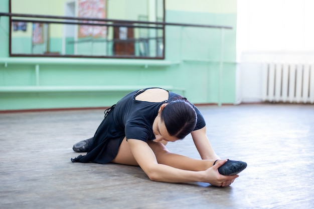 Giovane ballerina bruna che fa esercizi in studio di balletto