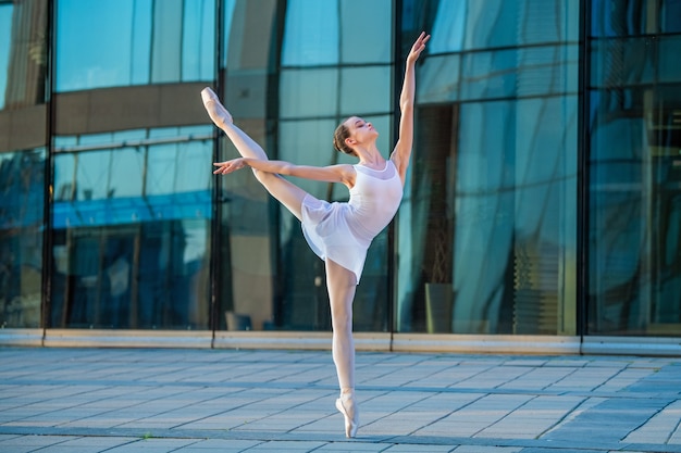 Giovane ballerina in un body bianco che balla su scarpe da punta sullo sfondo di un paesaggio urbano