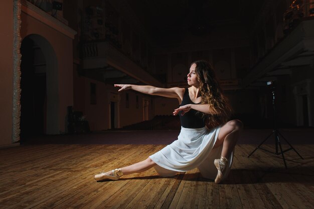 Giovane ballerina in una gonna bianca e scarpe da ballo su un palcoscenico teatrale La ballerina sta ballando su uno sfondo scuro