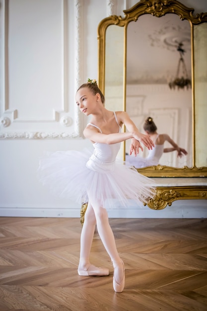 Giovane ballerina snella in tutù bianco balla sulle scarpe da punta in una stanza spaziosa e luminosa con grandi finestre.