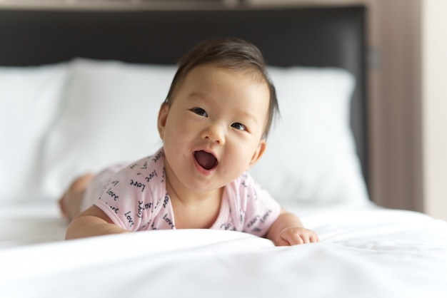 Giovane bambino asiatico sveglio che striscia sul letto in camera da letto.