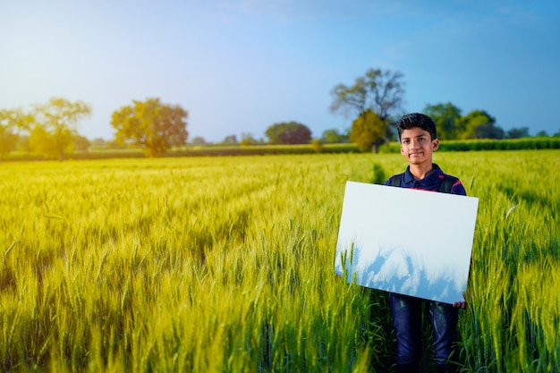 Giovane bambino indiano con poster bianco al campo di grano indiano