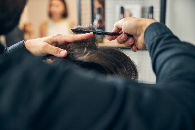 Giovane barbiere concentrato che usa strumenti sterili mentre crea un taglio di capelli alla moda per il suo cliente