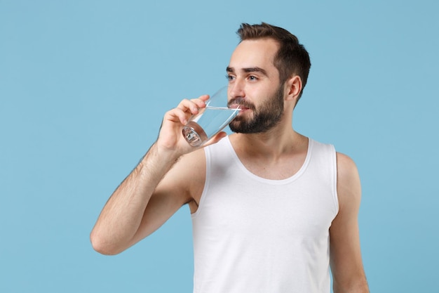 Giovane barbuto 20 anni pelle perfetta in camicia bianca tenere acqua isolata su sfondo blu pastello muro, ritratto in studio. Concetto di procedure cosmetiche sanitarie per la cura della pelle. Simula lo spazio della copia.