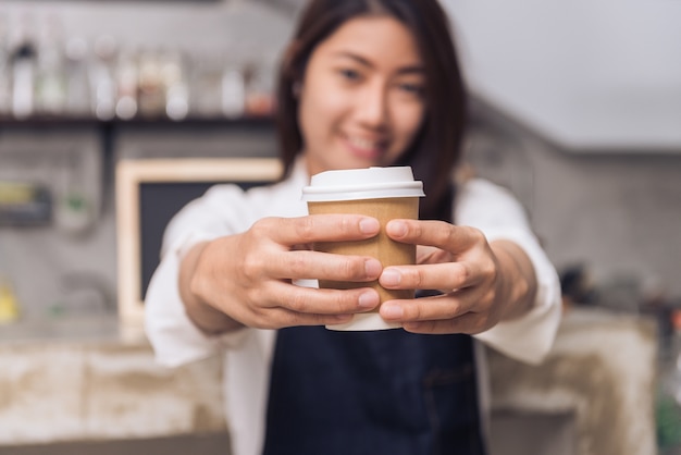 Giovane barista asiatico della donna che tiene una tazza di caffè a gettare con il fronte sorridente al fondo del caffè